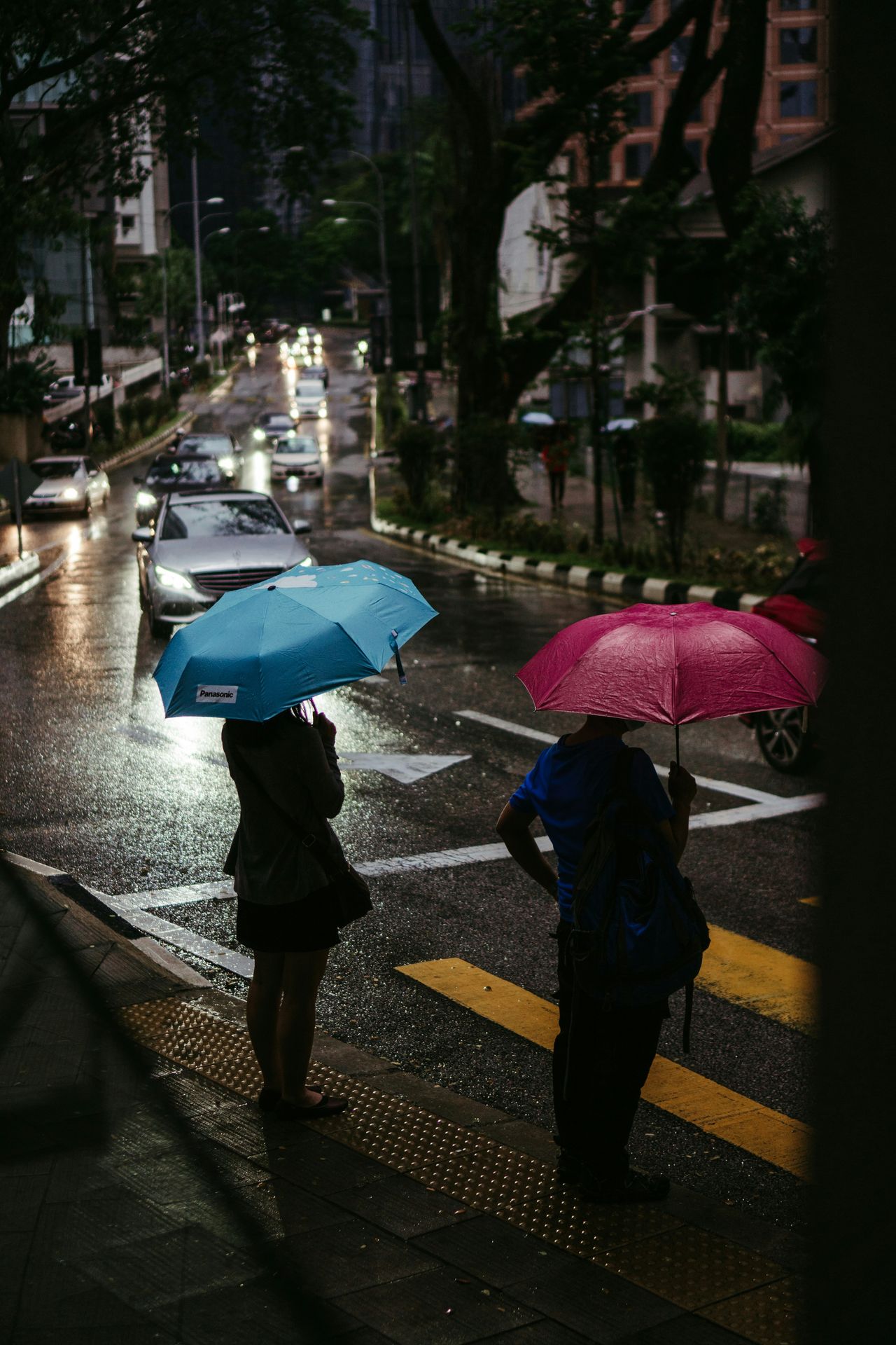 Pedestrians walking with umbrellas on a wet sidewalk in Kuala Lumpur, Malaysia, during a tropical rain shower.